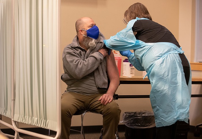 A person in a grey sweatshirt getting vaccinated by a nurse