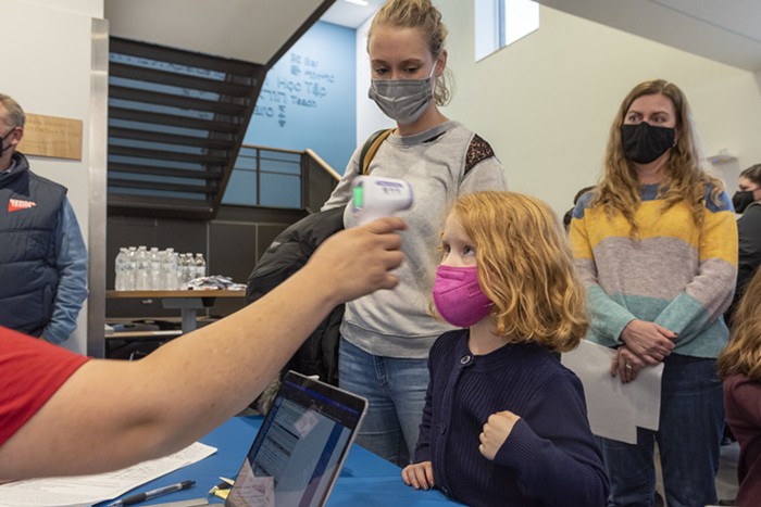 A young girl gets her temperature checked at a check-in table.